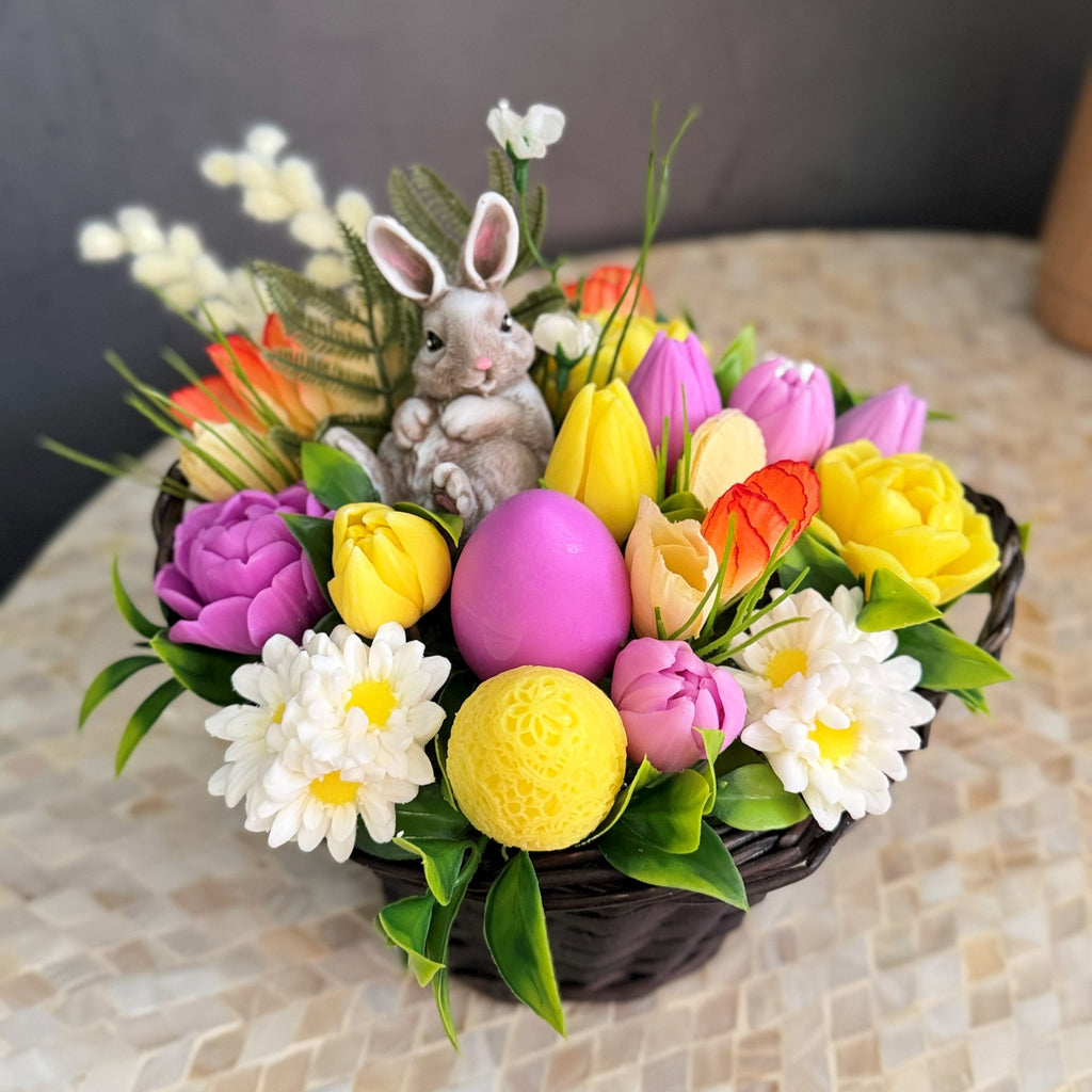Colorful Easter-themed flower arrangement with eggs and a rabbit figurine on a textured surface.
