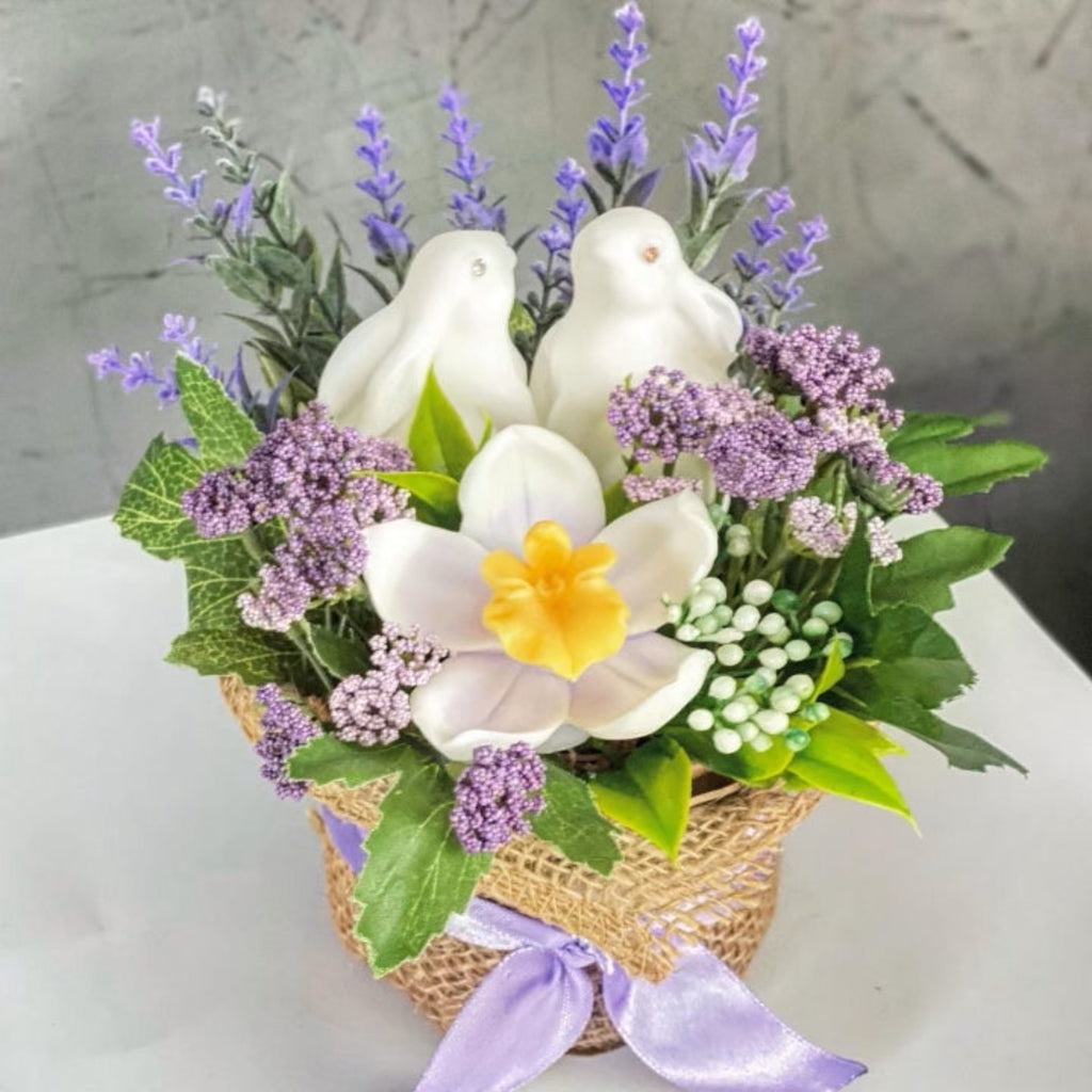 Floral arrangement with white doves, purple flowers, and a yellow flower on a gray background