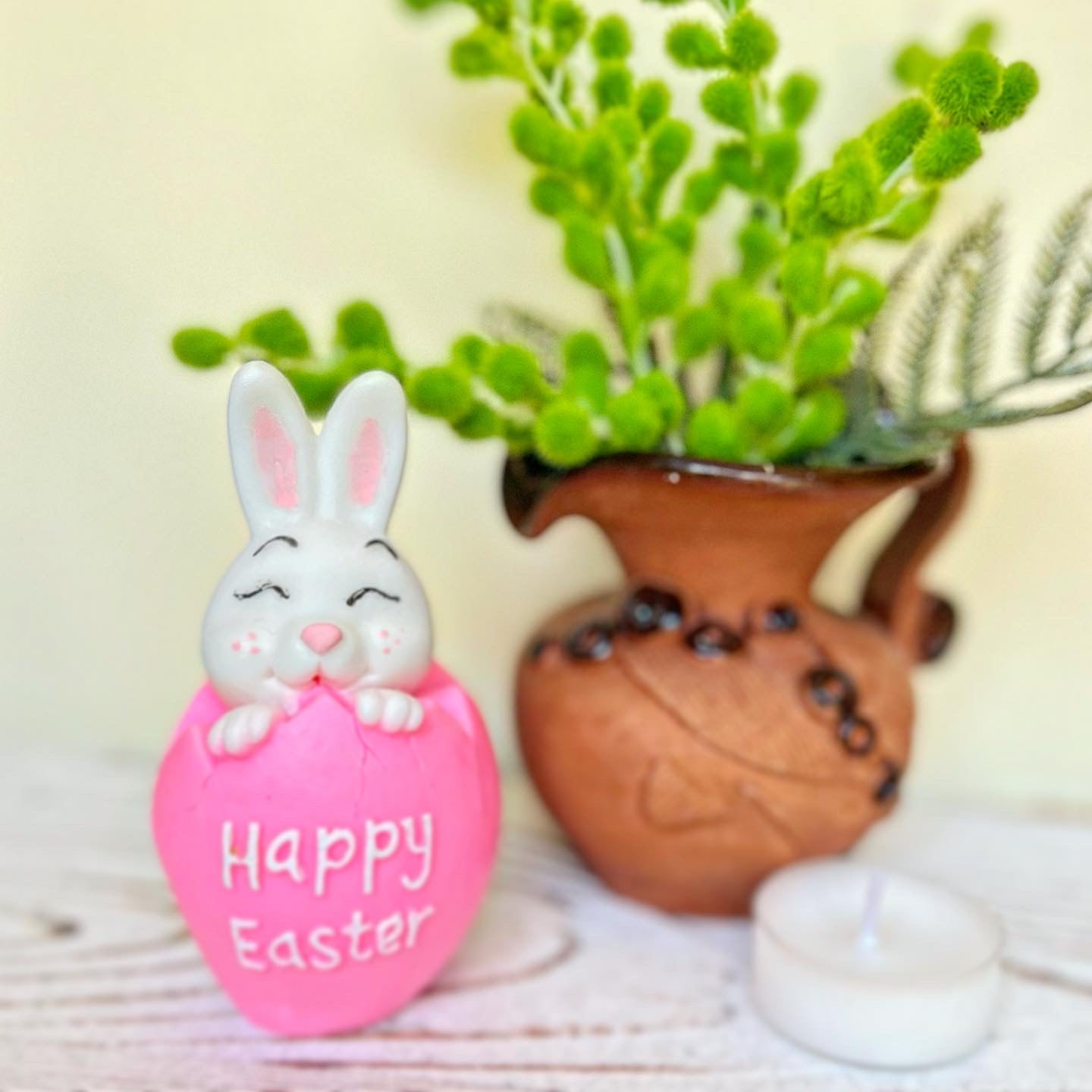 Decorative Easter egg with a bunny on top, featuring 'Happy Easter' text, in front of a plant.