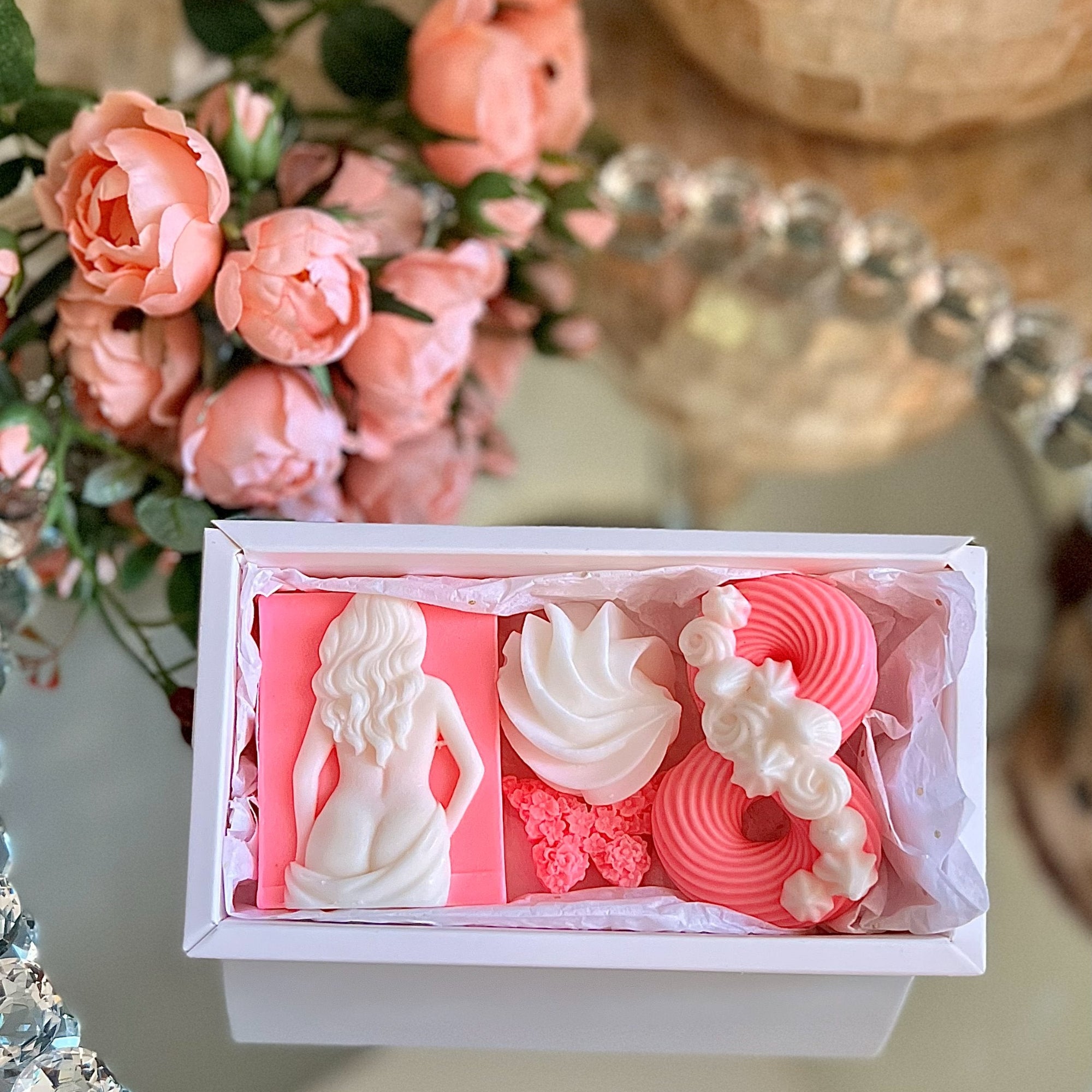 Decorative soap set in a box with pink and white designs, surrounded by flowers and a decorative mirror.