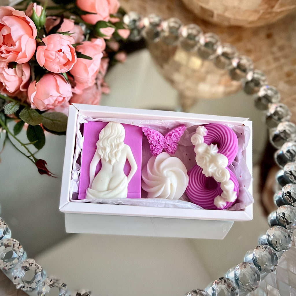 Decorative box with figurines, flowers, and a butterfly on a reflective surface with a floral arrangement in the background.