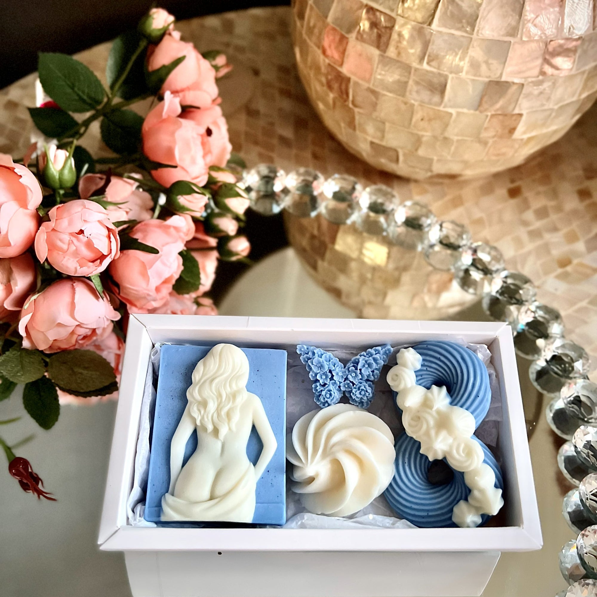 Decorative items including a figurine, butterfly, and swirls in a box on a table with flowers and a mirror.