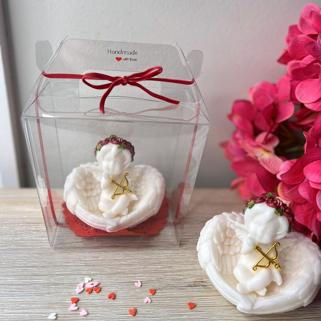 Two white angel figurines with red ribbons on a wooden surface with pink flowers in the background.