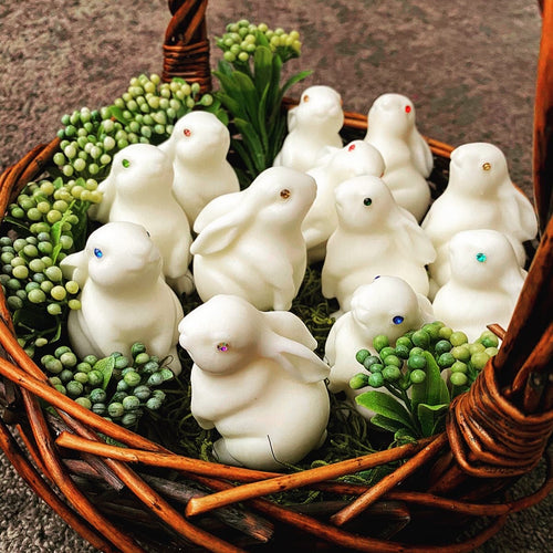 White rabbit-shaped candles in a woven basket with greenery