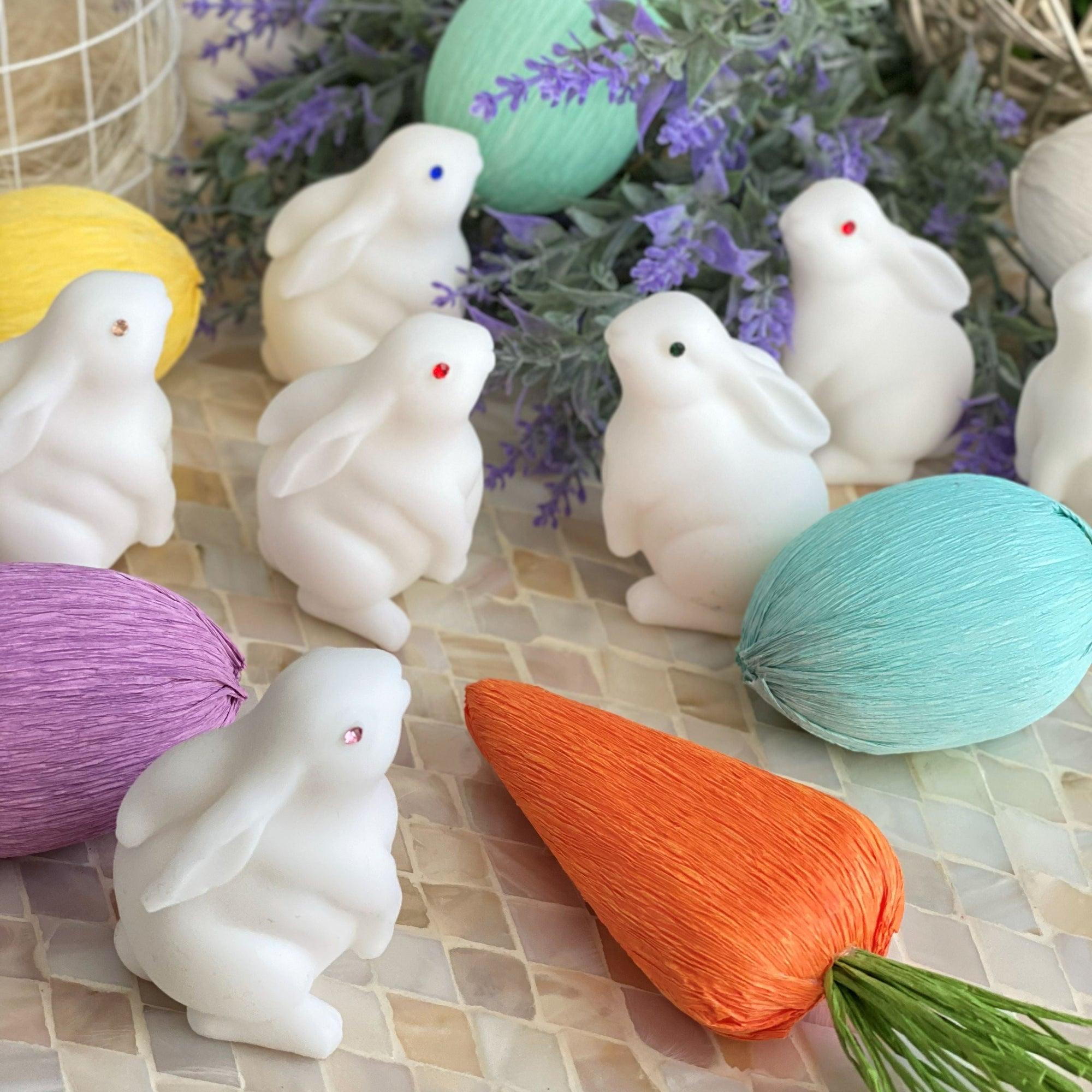 White rabbit-shaped candles with colorful eggs and a carrot on a decorative surface.