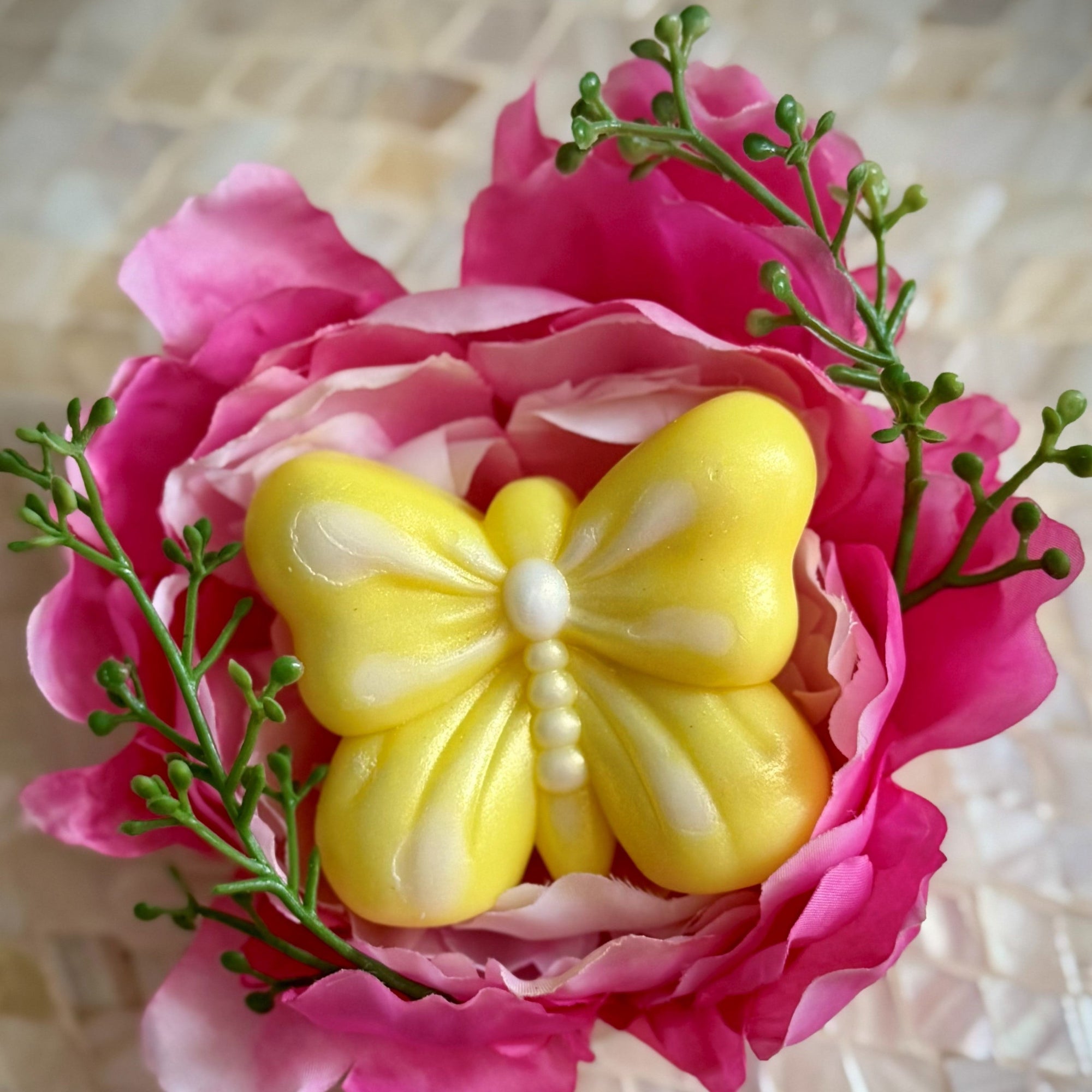 Hand holding a pink butterfly-shaped handmade soap wrapped in clear cellophane and tied with a white ribbon.
