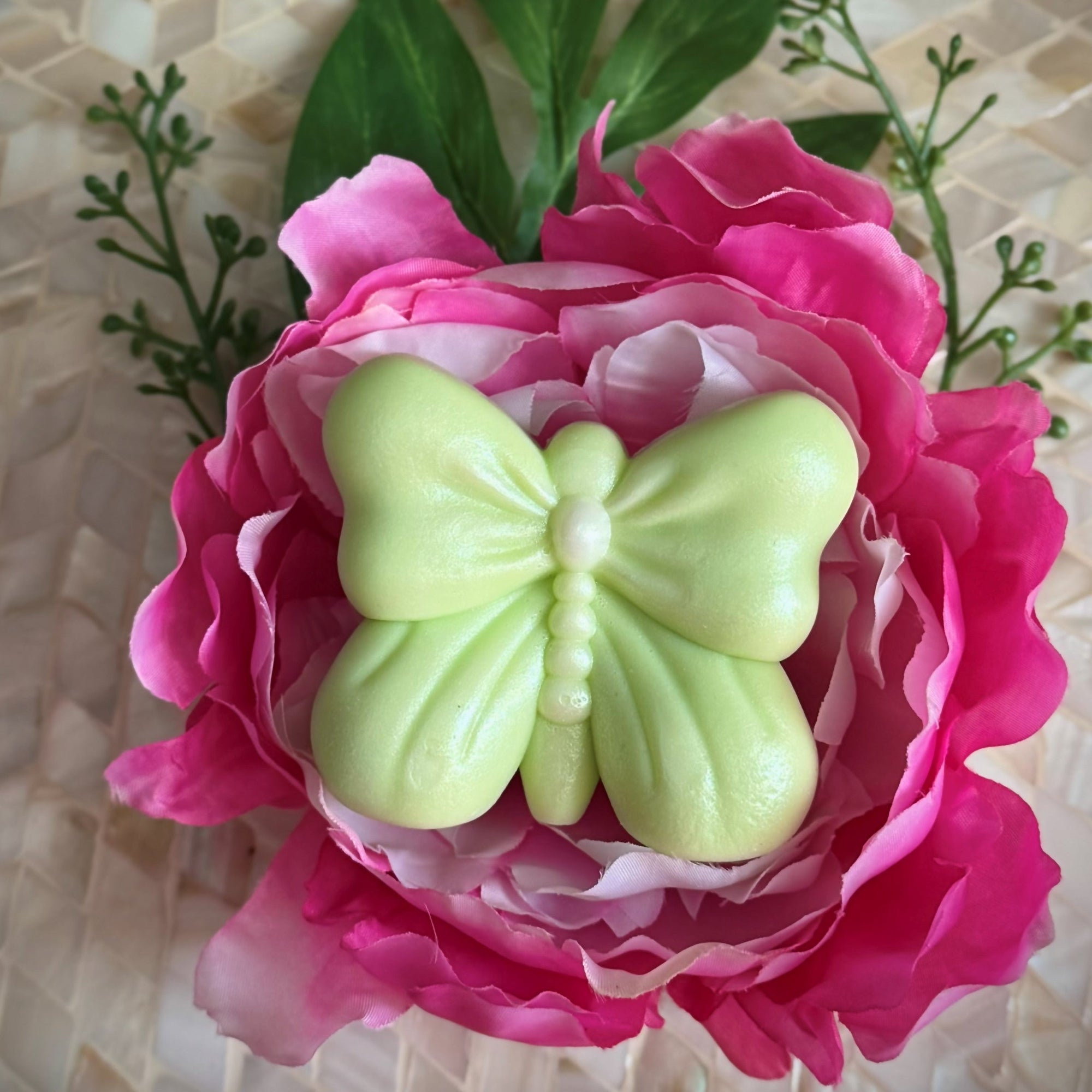Pink flower with a green butterfly-shaped object on a textured surface