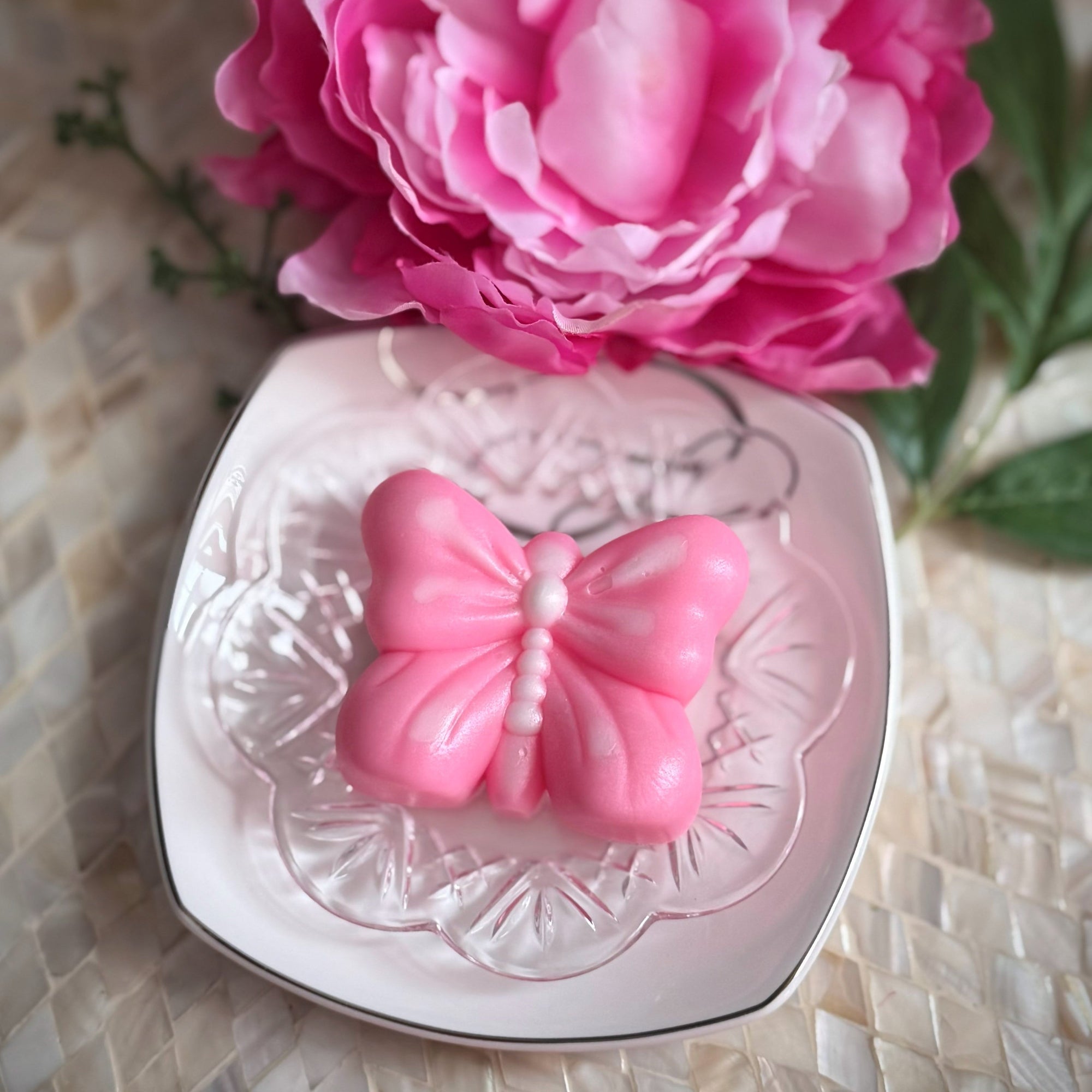 Pink butterfly-shaped object on a decorative plate with pink flowers in the background