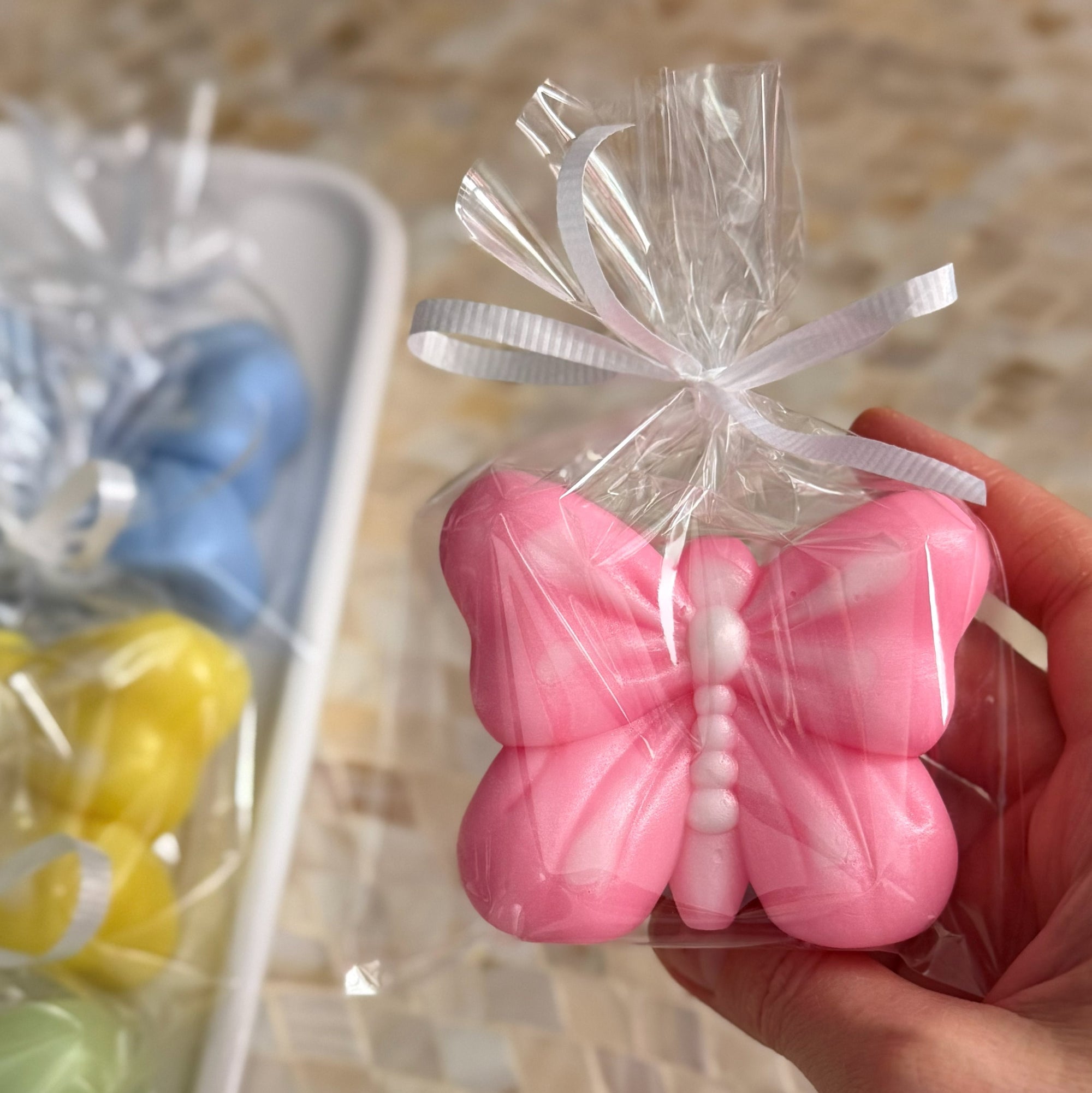 Pink butterfly-shaped candy in clear packaging held by a hand on a tiled floor.