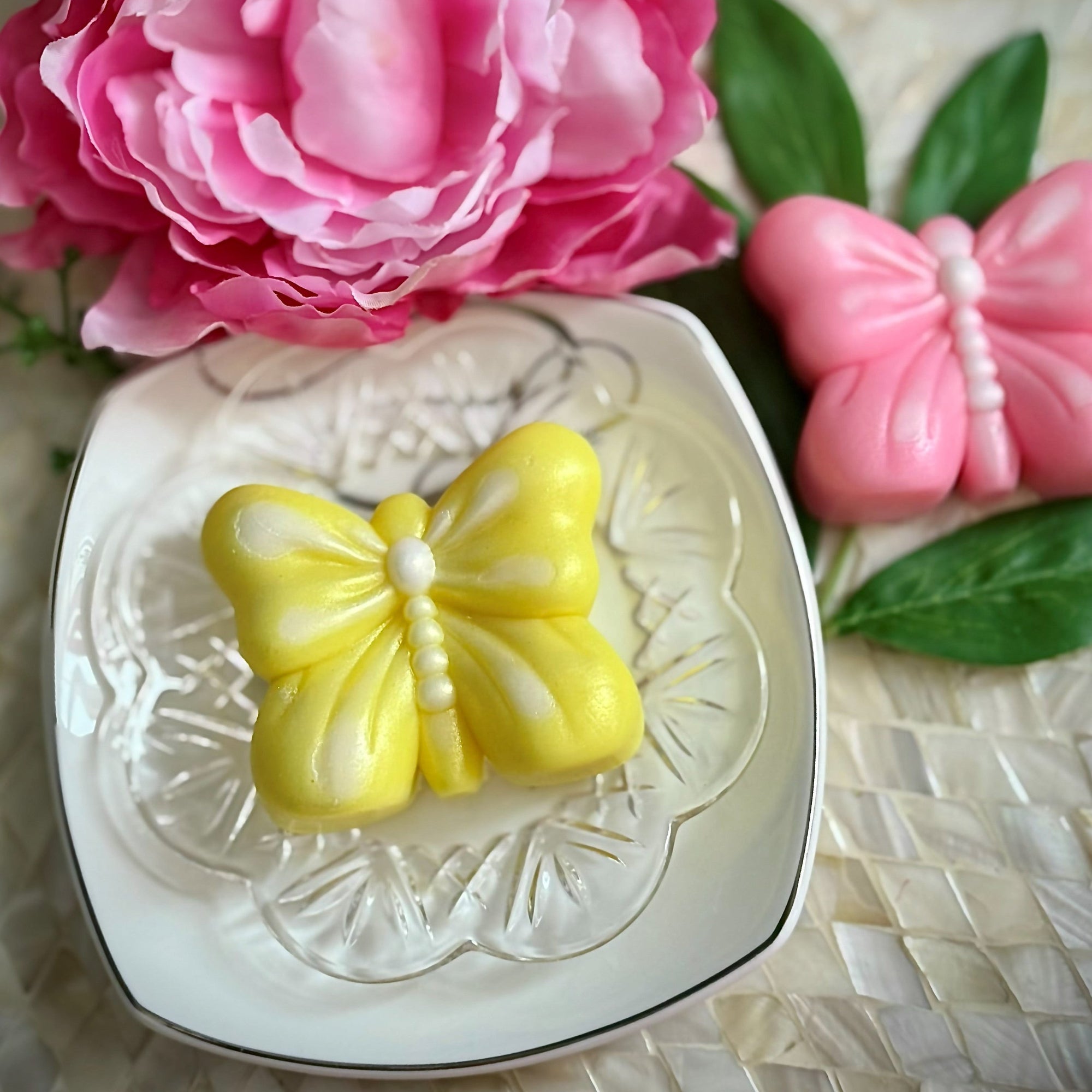 Yellow butterfly soap on a decorative plate with pink flowers and green leaves in the background.