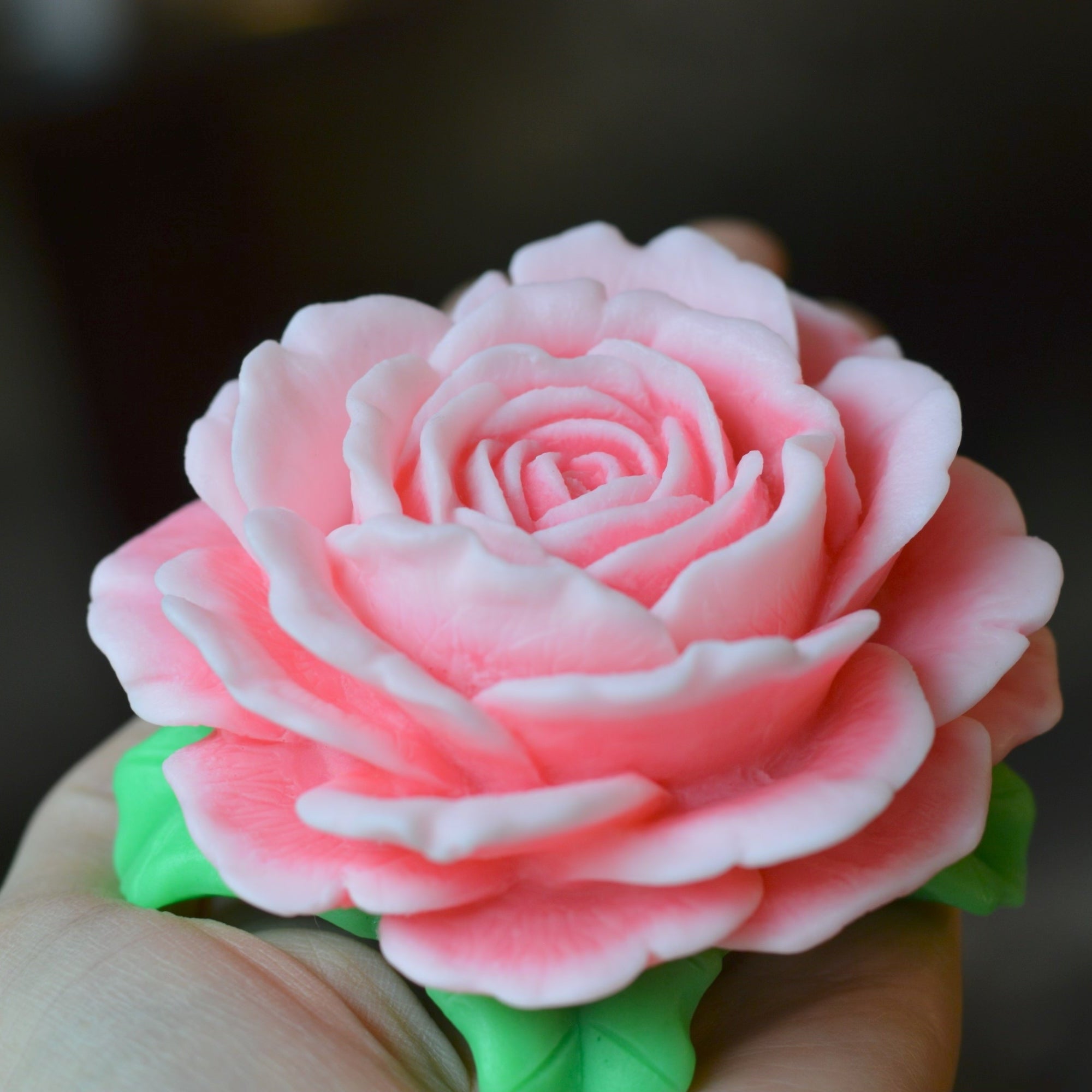Pink rose made of fondant held by a hand against a blurred background