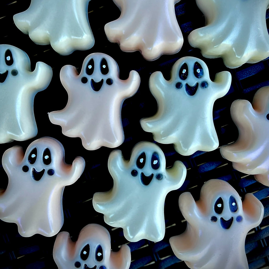 Ghost-shaped white chocolate candies with black eyes and smiles, arranged on a dark cooling rack.